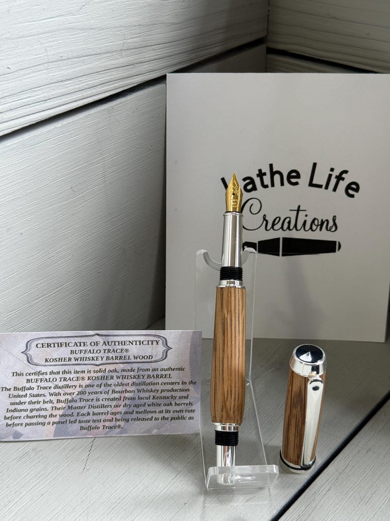 May include: A handcrafted fountain pen with a wooden barrel and silver accents. The pen features a gold nib and a matching cap. A certificate of authenticity is visible, along with the text "athe Life Creations".