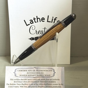Pu&ograve; includere: Una penna in legno con dettagli neri, presentata su un supporto trasparente. La penna &egrave; realizzata in legno di botte di whisky Buffalo Trace Kosher. Un certificato di autenticit&agrave; e un cartello con il testo "Lathe Life Creat" sono sullo sfondo.