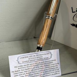 May include: A wooden pen with a silver clip and accents, made from Buffalo Trace Kosher Whiskey Barrel wood. The pen is displayed with a certificate of authenticity.