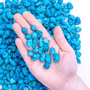 Peut inclure: Une main tenant un tas de pierres bleu turquoise. Les pierres sont lisses et ont un aspect naturel et poli.