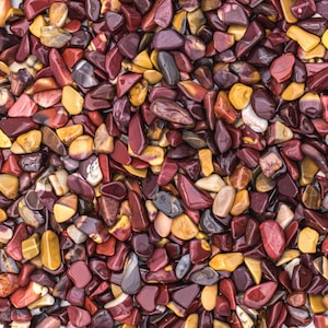 May include: A close-up view of a collection of polished stones in shades of red, burgundy, yellow, and brown. The stones vary in size and shape, with a glossy finish. The arrangement creates a textured, natural pattern.