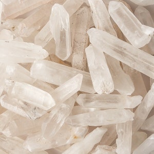 May include: A collection of clear quartz crystal points, also known as rock crystals. The points are various sizes and shapes, with some having a natural, cloudy appearance.