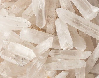 May include: A collection of clear quartz crystal points, also known as rock crystals. The points are various sizes and shapes, with some having a natural, cloudy appearance.