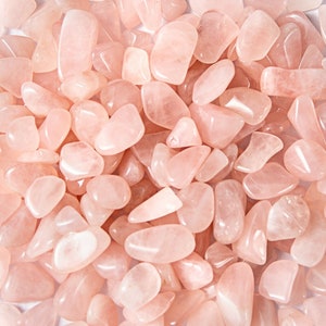 May include: A close-up of a pile of pink rose quartz tumbled stones. The stones are smooth and polished, with a natural, light pink color.