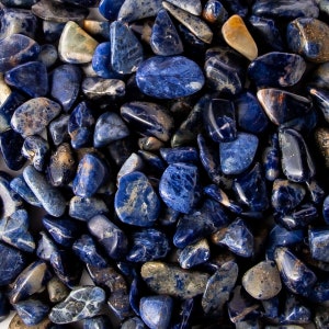 May include: A collection of tumbled blue sodalite stones. The stones are various sizes and shapes, with a smooth, polished finish.