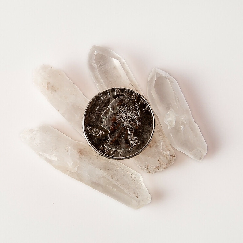 Puede incluir: Cuatro puntas de cristal de cuarzo transparente dispuestas alrededor de una moneda de veinticinco centavos de d&oacute;lar estadounidense de plata con el a&ntilde;o 1997 visible. La moneda dice "Liberty" e "In God We Trust".