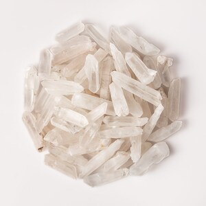 Puede incluir: Un mont&oacute;n de puntas de cristal de cuarzo transparente, tambi&eacute;n conocidas como cristales de roca, sobre un fondo blanco. Los cristales son de varios tama&ntilde;os y formas, algunos son largos y delgados, mientras que otros son m&aacute;s cortos y gruesos.
