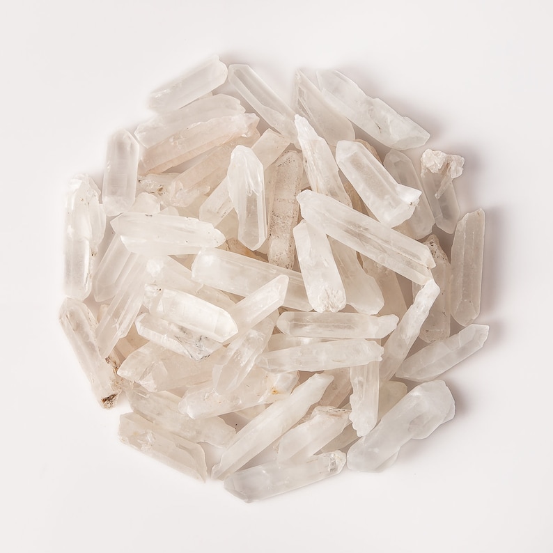 Puede incluir: Un mont&oacute;n de puntas de cristal de cuarzo transparente, tambi&eacute;n conocidas como cristales de roca, sobre un fondo blanco. Los cristales son de varios tama&ntilde;os y formas, algunos son largos y delgados, mientras que otros son m&aacute;s cortos y gruesos.