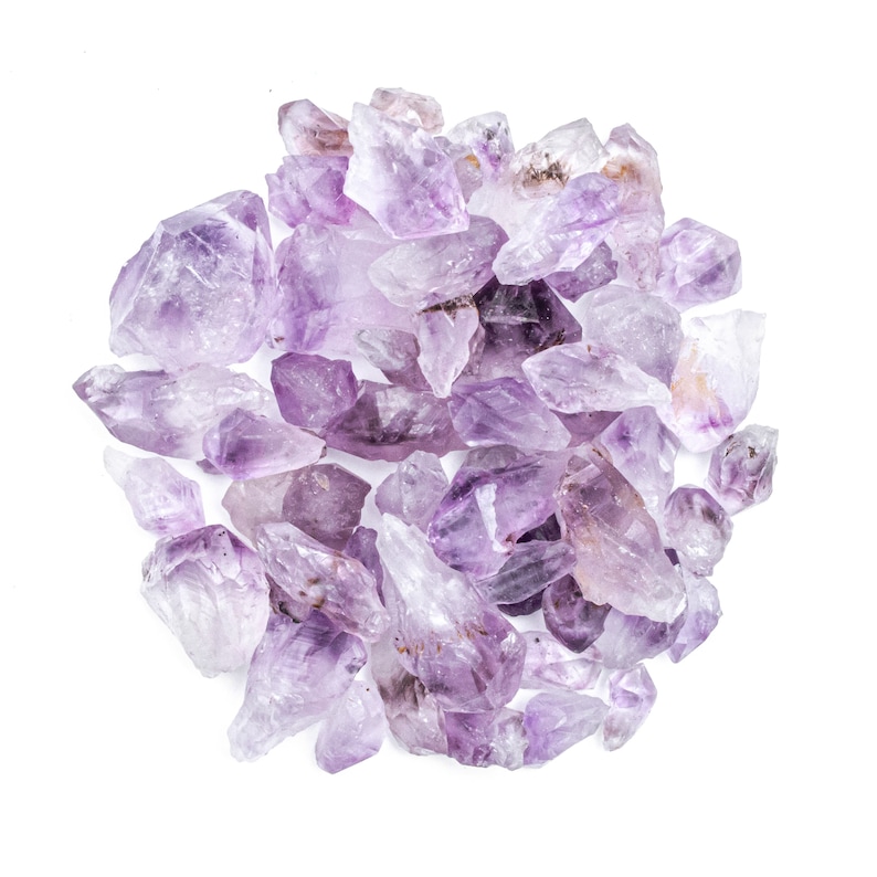 May include: A cluster of amethyst crystals, ranging in size and shape, with a purple hue. The crystals are arranged in a circular pattern on a white background.