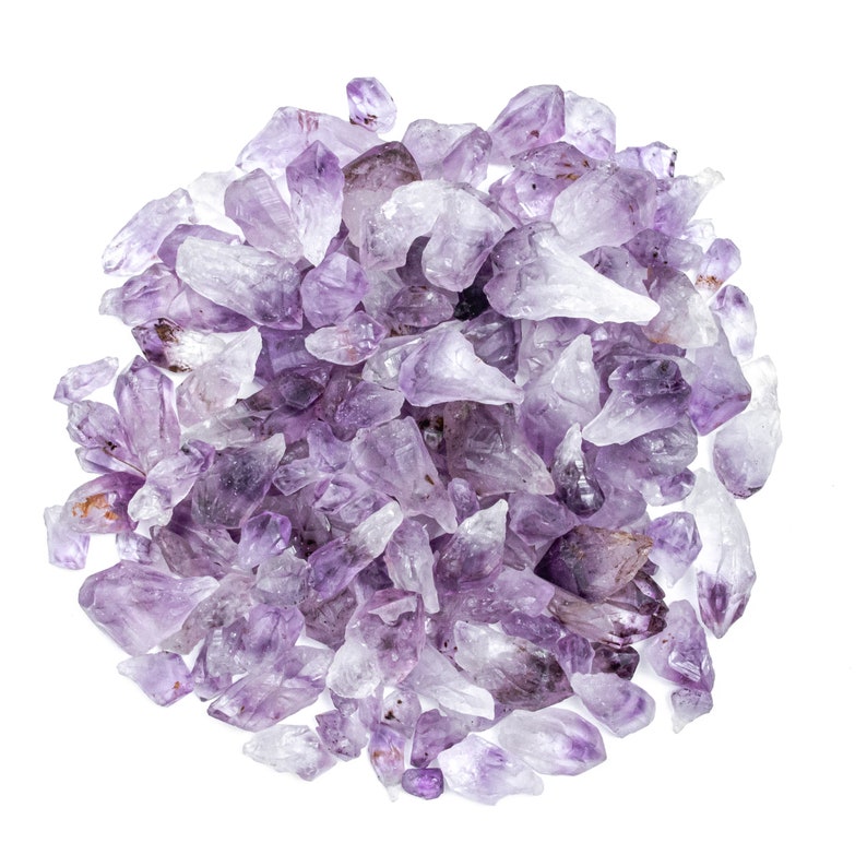 May include: A large pile of amethyst crystals, ranging in size and shape, with a purple hue. The crystals are scattered on a white background.