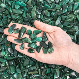May include: A hand holding a collection of green aventurine tumbled stones. The stones are smooth and polished, and they are surrounded by more of the same stones.