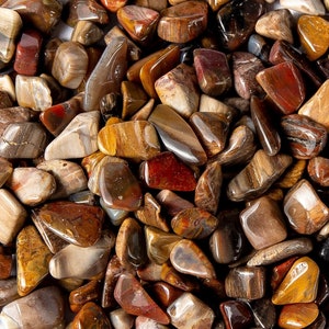 May include: A close-up of a collection of polished, tumbled stones in shades of brown, red, and gold. The stones have a variety of shapes and sizes, and they are arranged in a random pattern.