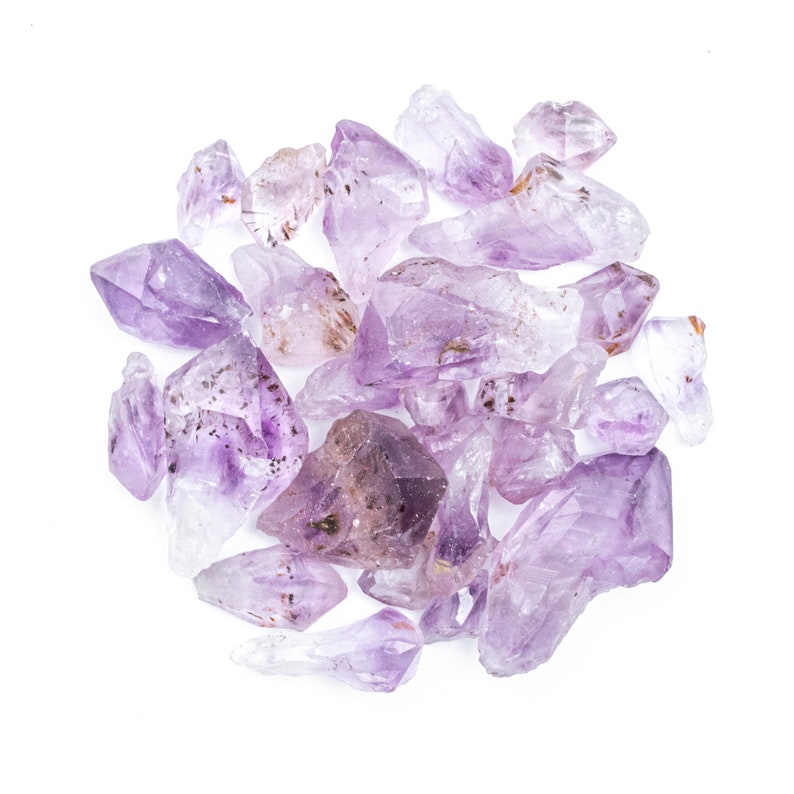 May include: A collection of amethyst crystals in various sizes and shapes, ranging from light to deep purple hues. The crystals are arranged in a cluster on a white background.