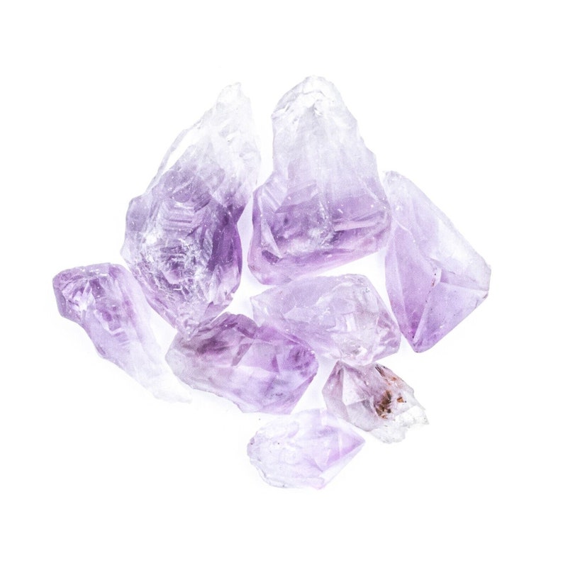 May include: A group of amethyst crystals in various shapes and sizes. The crystals are a light purple color and have a translucent appearance.