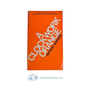 May include: A Clockwork Orange book cover in orange with white text. The title is in a diagonal layout, with the author's name at the bottom. The text includes "Stanley Kubrick's first motion picture since 2001: A SPACE ODYSSEY".