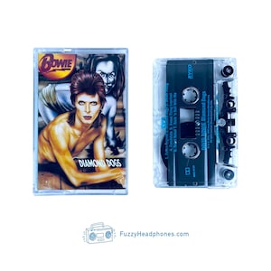 May include: A vintage cassette tape featuring the album "Diamond Dogs" by David Bowie. The cover art shows a portrait of Bowie with the album title. The cassette is in a clear plastic case. The website FuzzyHeadphones.com is visible.