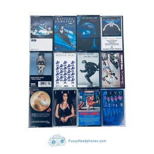 Peut inclure: Une collection de douze cassettes audio vintage avec des pochettes d'albums vari&eacute;es. Les cassettes pr&eacute;sentent des couleurs et des illustrations diverses, avec des images de musiciens et de logos de groupes. Le texte "FuzzyHeadphones.com" est inclus.