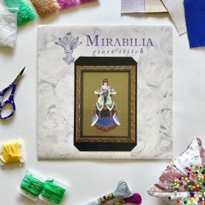 Può includere: Un modello a punto croce di Mirabilia con un'immagine incorniciata di una donna in un abito dettagliato. L'immagine è circondata da forniture per punto croce, tra cui filo, perline, forbici e un cuscinetto per spilli.