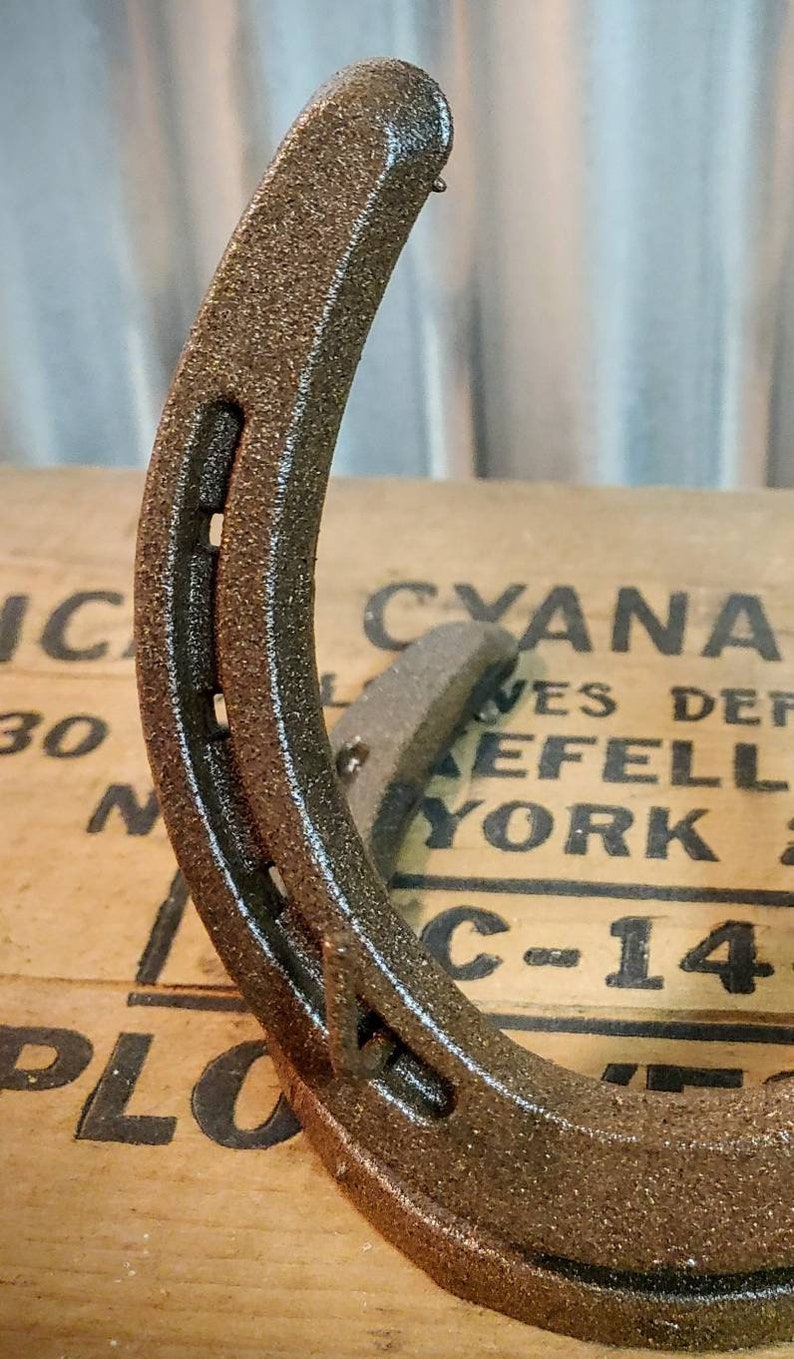 May include: A rustic brown horseshoe with a rough, textured surface. The horseshoe is lying on a wooden surface with the text "CYANAMID" and "C-14" visible.