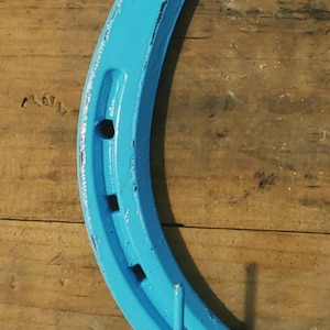 May include: A blue horseshoe with two hooks attached to the bottom. The horseshoe is painted a light blue color and has a distressed finish.