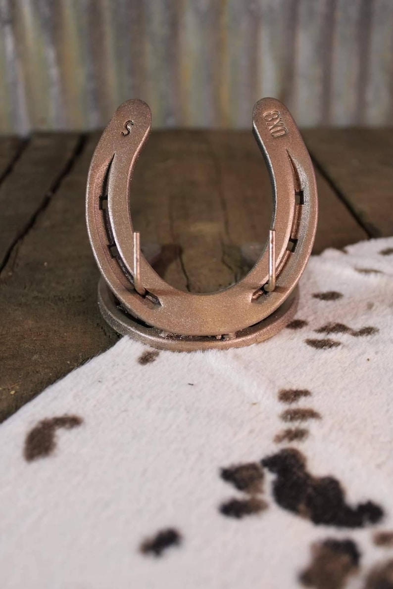 May include: A gold-colored horseshoe with the number "8" and the letter "S" engraved on it. The horseshoe is on a white and brown cowhide rug.
