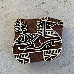 Könnte beinhalten: Ein geschnitzter Holzblock mit einem Pferdemotiv. Das Pferd ist in einem stilisierten, volkstümlichen Stil mit weißen Linien auf dunklem Braun dargestellt. Der Block ist rechteckig mit abgerundeten Kanten und dient wahrscheinlich zum Drucken.