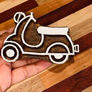 Può includere: Un'incisione su legno di uno scooter in uno schema di colori marrone e bianco. Lo scooter è delineato in bianco e lo sfondo è marrone.