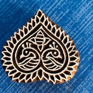 Puede incluir: Un sello de impresión de madera con un diseño en forma de corazón. El diseño presenta intrincados patrones florales y remolinos en color marrón oscuro sobre un fondo marrón claro.