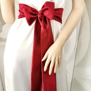 May include: A red satin sash tied in a bow around the waist. The sash is a simple, elegant accessory for a wedding or special occasion.