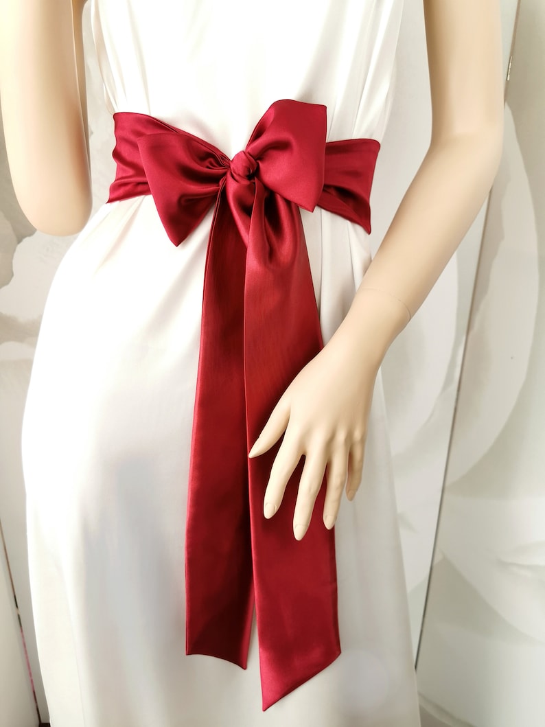 May include: A red satin sash tied in a bow around the waist. The sash is a simple, elegant accessory for a wedding or special occasion.