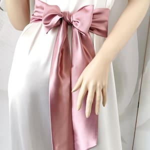 May include: A dusty rose satin ribbon tied in a bow around the waist. The ribbon is tied in a large bow with long tails.