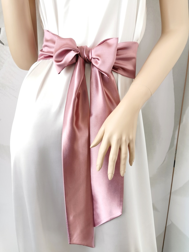 May include: A dusty rose satin ribbon tied in a bow around the waist. The ribbon is tied in a large bow with long tails.