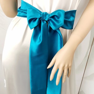 May include: A turquoise satin ribbon tied in a bow around a white dress.