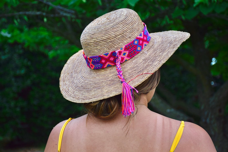 May include: A straw hat with a wide brim and a colorful woven band. The band has a pink tassel hanging from it.