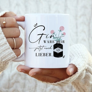 Könnte beinhalten: Weiße Keramiktasse mit einer schwarz-weißen Illustration einer Gin-Flasche und rosa Blumen. Der Text auf der Tasse lautet "Gin ware mir jetzt auch lieber."