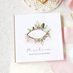 Könnte beinhalten: Weißes Fotoalbum mit einer goldenen Fischillustration, umgeben von grünen und braunen floralen Elementen. Der Text "marleen" und "Meine Taufe am 25.05.2024" ist auf dem vorderen Umschlag gedruckt.