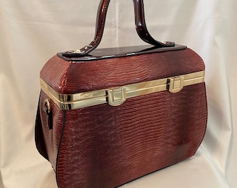 May include: A burgundy faux leather handbag with a gold metal clasp and a top handle. The bag has a textured, crocodile-like pattern.