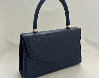 May include: A navy blue handbag with a textured finish. The bag features a curved handle and silver-toned metal accents. The flap closure adds a classic touch to this rectangular purse.