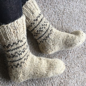 May include: A pair of beige wool socks with a black and white geometric pattern. The socks are knitted and have a fuzzy texture.