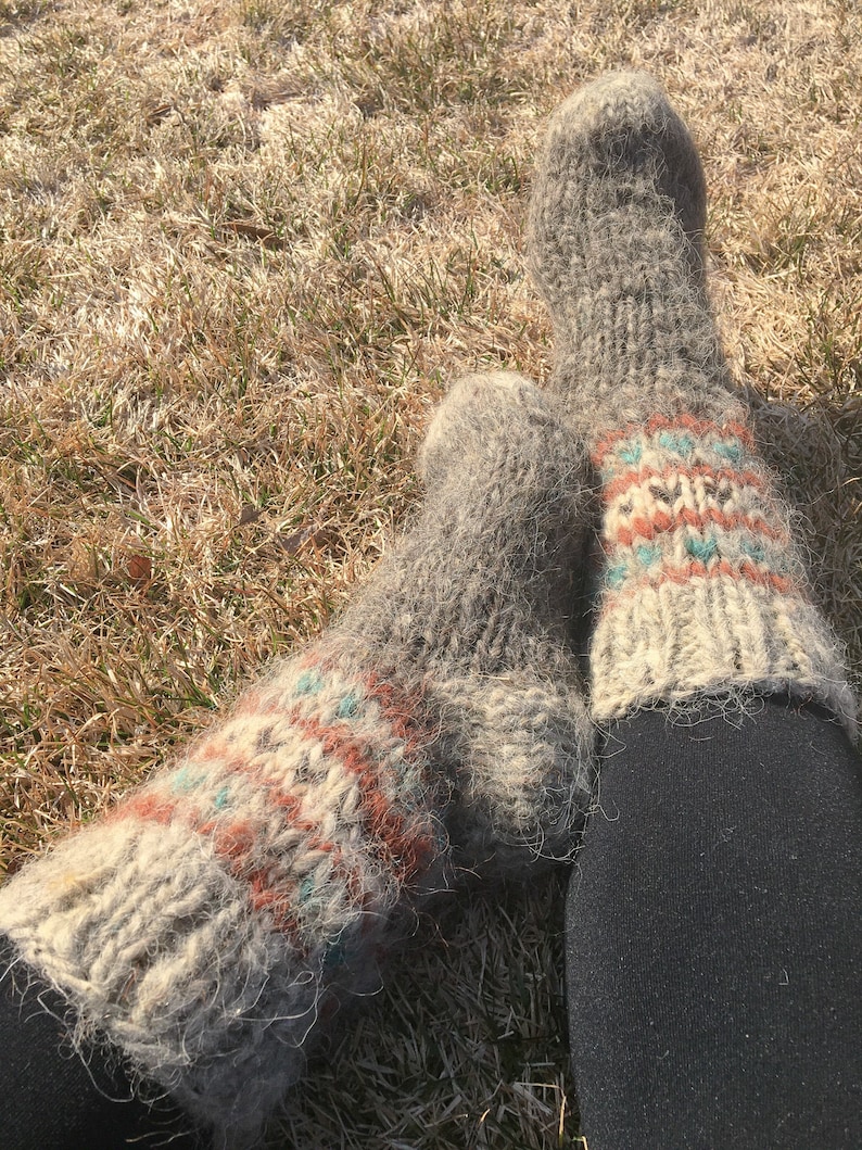 May include: A pair of grey wool socks with colourful geometric patterns. The socks are worn and have a fuzzy texture.