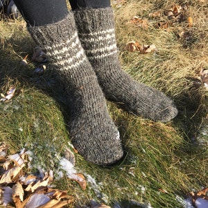 May include: A pair of gray wool socks with white stripes. The socks are worn and are sitting on a bed of green grass with brown leaves.