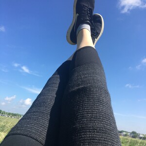 May include: A pair of black athletic shoes with white soles, worn by a person wearing black leggings with a textured pattern. The person is lying on their back with their legs in the air, against a bright blue sky with white clouds.