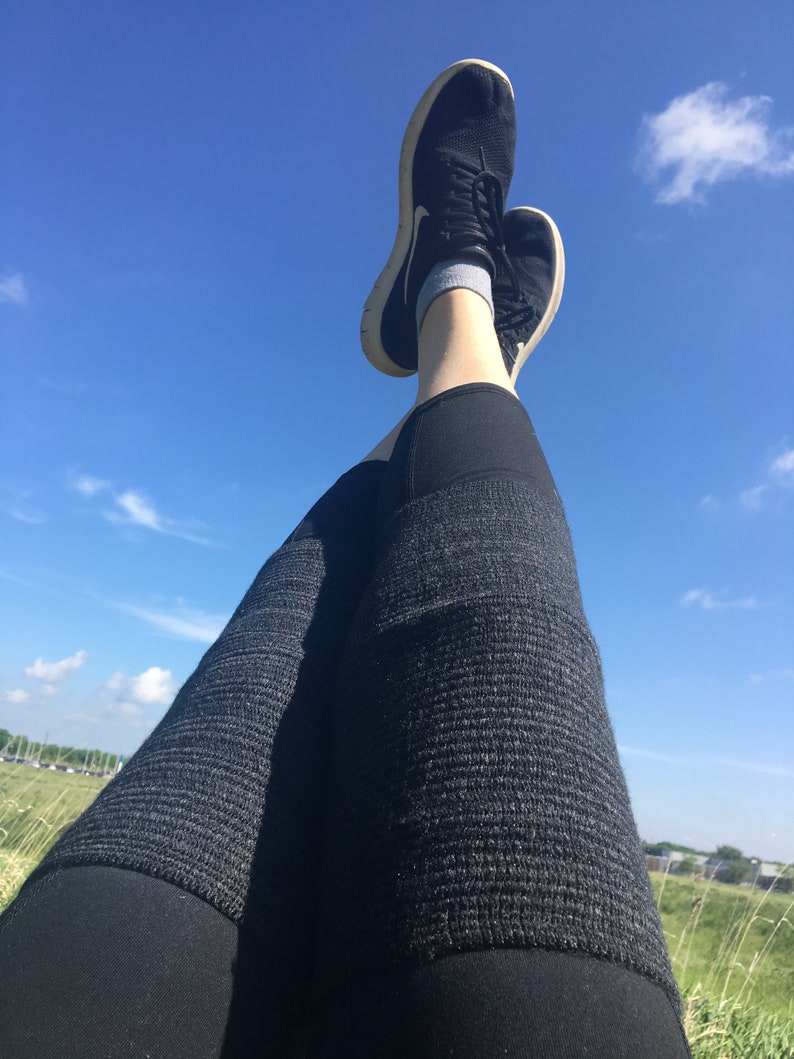 May include: A pair of black athletic shoes with white soles, worn by a person wearing black leggings with a textured pattern. The person is lying on their back with their legs in the air, against a bright blue sky with white clouds.