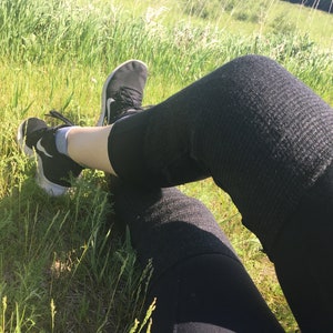 May include: A person wearing black leggings and black sneakers sits in a grassy field.