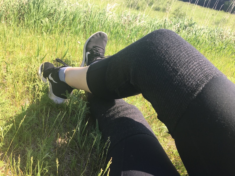 May include: A person wearing black leggings and black sneakers sits in a grassy field.