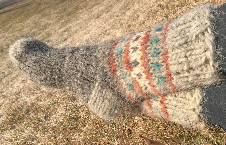 May include: A pair of grey and white wool socks with a colourful geometric pattern. The socks are knitted and have a fuzzy texture.