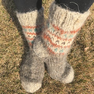 May include: A pair of fluffy, grey wool socks with a colourful geometric pattern. The socks are knitted with a thick yarn and have a fuzzy texture.