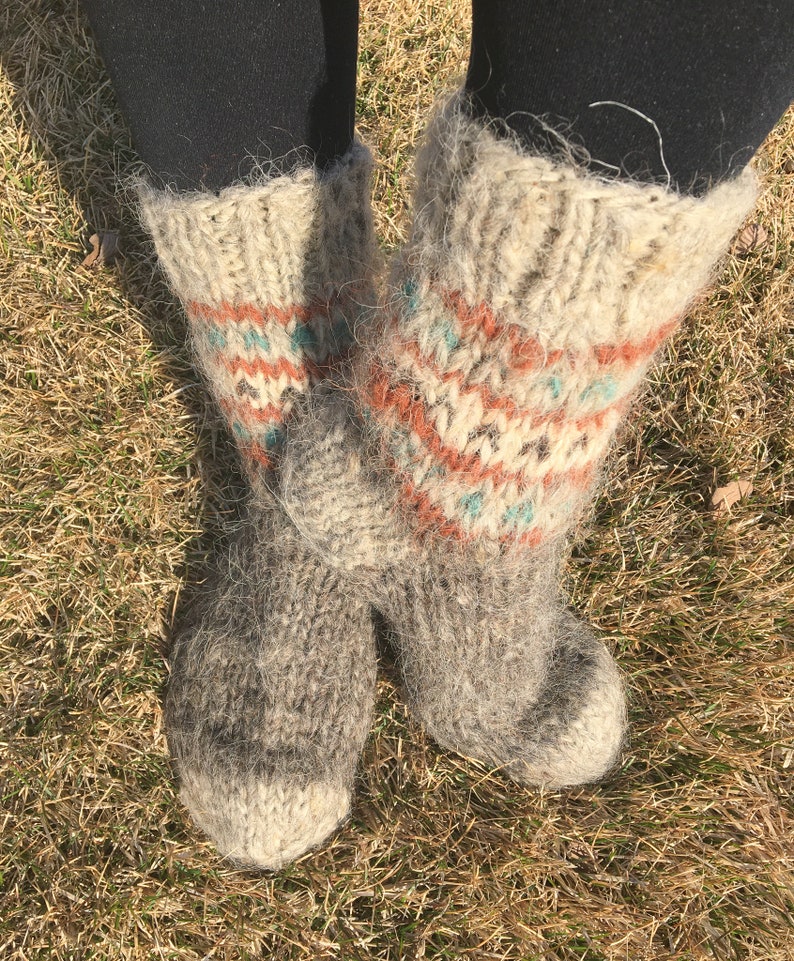 May include: A pair of fluffy, grey wool socks with a colourful geometric pattern. The socks are knitted with a thick yarn and have a fuzzy texture.