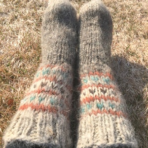 May include: A pair of thick, fuzzy, grey wool socks with a colourful geometric pattern in shades of orange, blue, and white. The socks are worn and have a rustic, handmade look.
