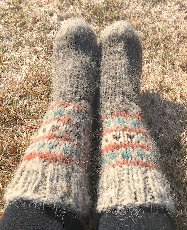 May include: A pair of thick, fuzzy, grey wool socks with a colourful geometric pattern in shades of orange, blue, and white. The socks are worn and have a rustic, handmade look.